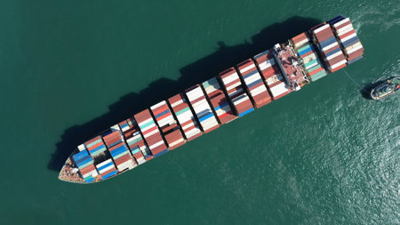 Aerial top view of large cargo ship filled with colorful containers in port area. Small tugboats assist in navigationの写真素材