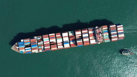Aerial top view of large cargo ship filled with colorful containers in port area. Small tugboats...
