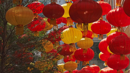 Vibrant red and yellow chinese lanterns hang overhead in a bustling street during a cultural festival celebrationの写真素材