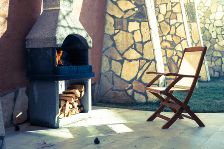 Outdoor stone fireplace in the shady backyard with the chair and firewoodの写真素材