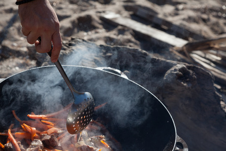 A man right arm is stewing meat with carrots in sunny day on a beachの写真素材
