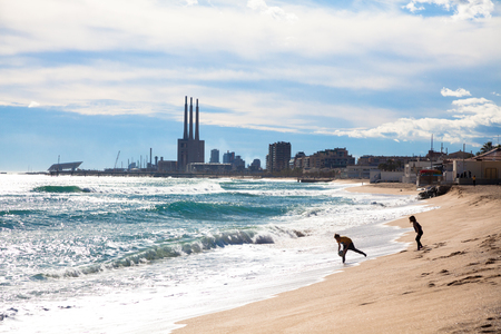 Sunny beach at the day with silhouettes of two young ones, white clouds and small buildings in the backgroundの写真素材