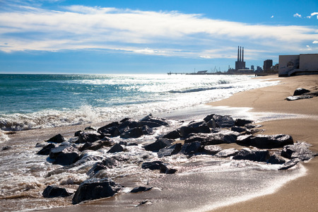 Sunny beach at the day with wet rocks, white clouds and small buildings in the backgroundの写真素材
