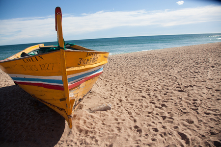 Yellow Boat lying on a sunny beach at the day with sea and white clouds in the backgroundの写真素材