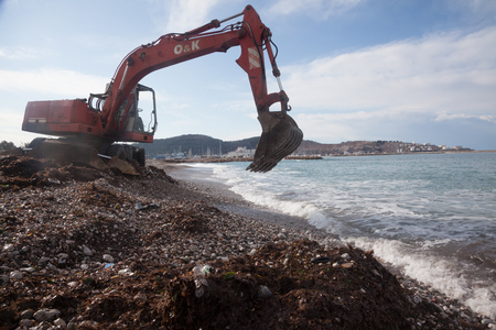 Urban services carried out a public beach cleaning before the tourist season start with the help of red excavatorのeditorial素材