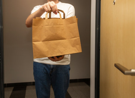 Delivery man holding a brown paper bag with food in front of the door