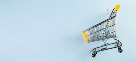 A yellow empty mini shopping cart on pastel blue background. Shopping concept.の写真素材