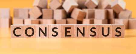 Consensus word on wooden cube blocks on yellow background with blurred cubes.の写真素材