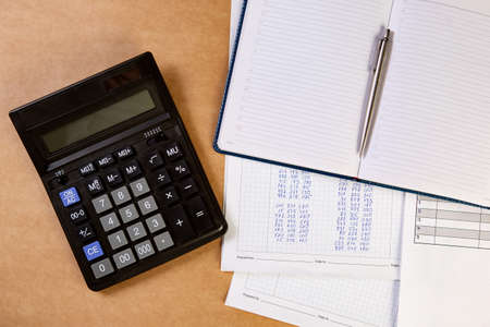 Flat lay of calculator with dairy, ballpoint pen and documents on the table.