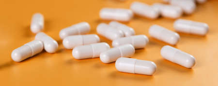 Pharmaceutical medicine white pills, tablets or capsules on yellow background.