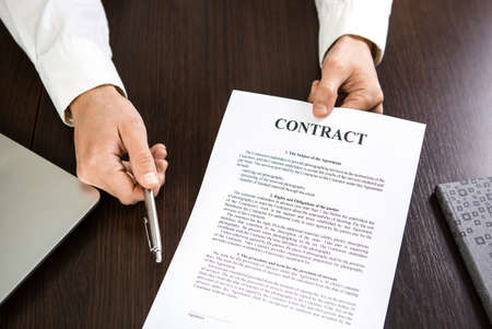 Businessman handing over a contract for signature offering a silver ballpoint pen in his hand.の写真素材