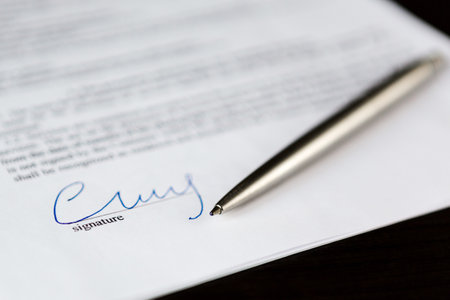 Closeup of signature and silver ballpoint pen with on document. Focus on signature.