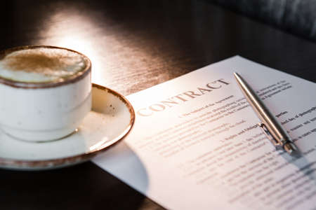 Cup of coffee with foam and cinnamon, ballpoint pen, blank contract on a wooden table.の写真素材