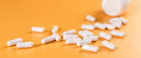 Pharmaceutical medicine white pills, tablets or capsules and bottle on yellow background.の写真素材