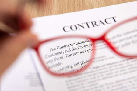 Close up of contract with red reading glasses in hand.の写真素材