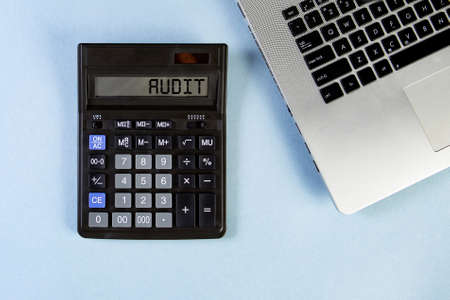 Calculator text AUDIT and laptop on the blue background. Top view.の写真素材