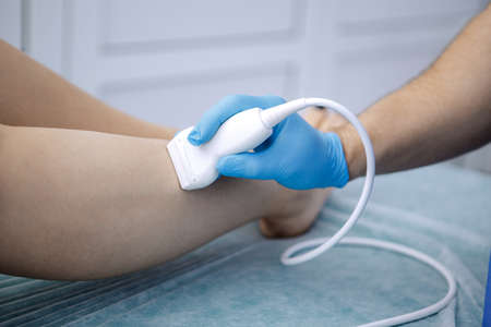 Physiotherapist is applying ultrasound therapy on the legs of a female patient.の写真素材