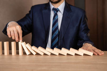 Businessman hand Stopping Falling wooden blocks. Dominoes effect. Strategy and successful intervention concept for business.の写真素材
