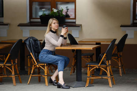 Beautiful and young girl in a jacket sitting in city cafe and laughing. Summer.の写真素材