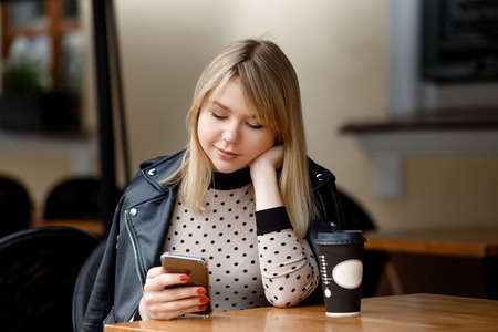 Happy smiling young woman using smartphone sitting in city cafeの写真素材