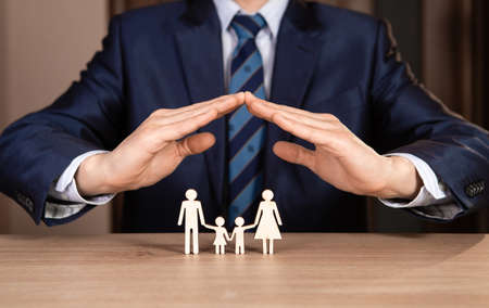 A man in a suit holds hands in the shape of a house over the family. Insurance concept.の写真素材