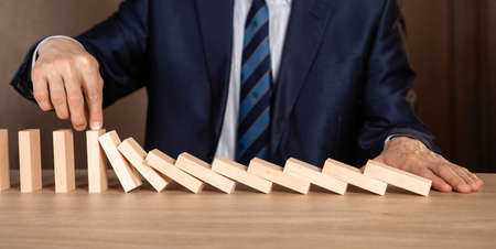 Businessman hand Stopping Falling wooden Dominoes effect from continuous toppled or risk, strategy and successful intervention concept for business.の写真素材