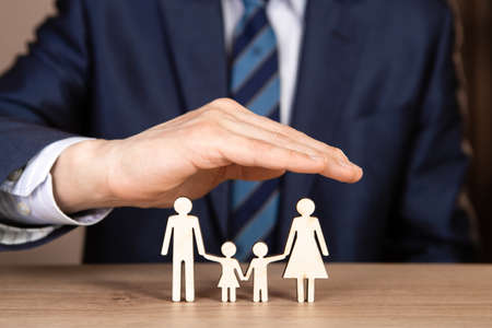 A man in a suit holds hands in the shape of a house over the family. Insurance concept.の写真素材