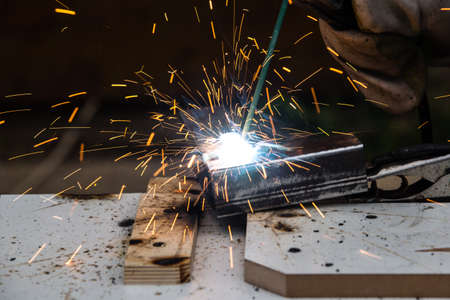 A welder welds a metal piece and many sparks from welding fly in different directionsの写真素材