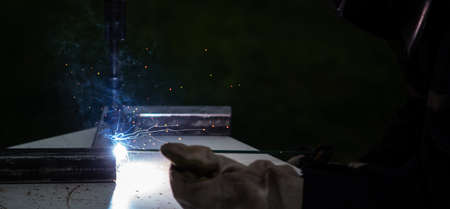 Metal welder working with arc welding machine to weld steel at factory while wearing safety equipment.の写真素材