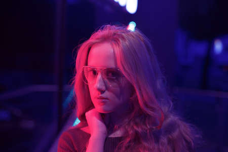 Beautiful portrait of young women in glasses near a red and blue neon sign in a cafe.