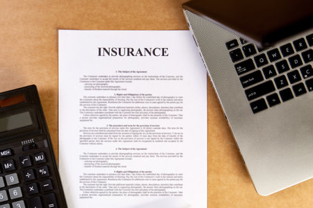 Flat lay of insurance policy with laptop and calculator on the wooden table.の写真素材