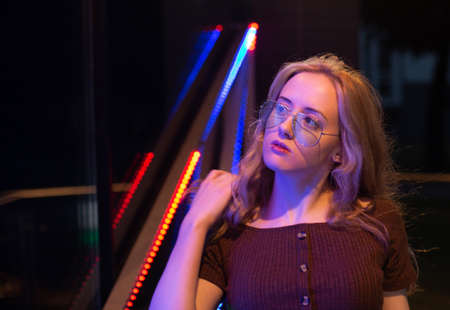 Portrait of a modern young girl with glasses, illuminated by red and blue neon light. Night city.の写真素材