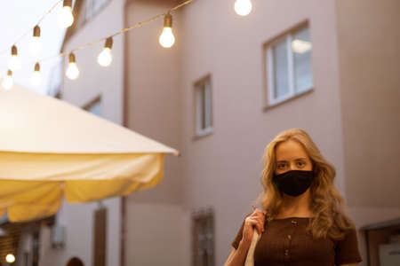 Beautiful girl with light hair in a black medical mask walking in the evening cityの写真素材