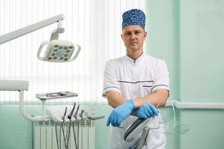 Highly qualified male dentist standing at his clinic with his arms crossed near modern dental equipment.の写真素材