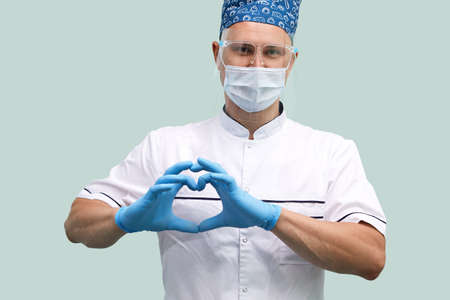 Doctor hands in gloves in the heart shape against the background of his body and medical gown. Male hand in blue medical gloves show heart sign.の写真素材
