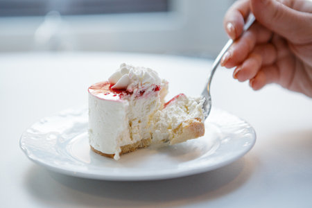 Close up red and white cake on plate being cut with fork in female hand.