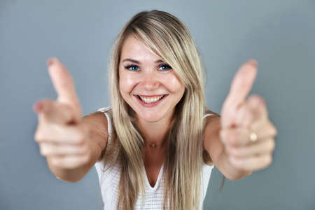 Smiling pretty young woman with blonde hair showing thumbs up isolated on the blue background.