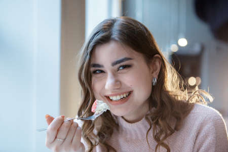Smiling young woman eating a sweet dessert in cafe. Close-up portrait.の写真素材
