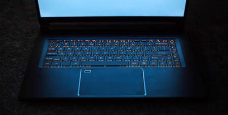 Laptop keyboard with orange neon illumination, backlit keyboard. Black laptop with blue monitor.の写真素材
