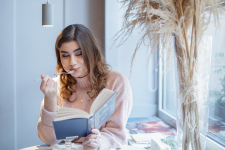 Women sits in cafe, eats cake and reads a book.の写真素材