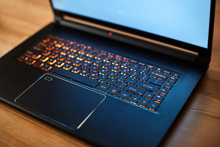 Laptop keyboard with orange neon illumination, backlit keyboard. Black laptop with blue monitor.の写真素材