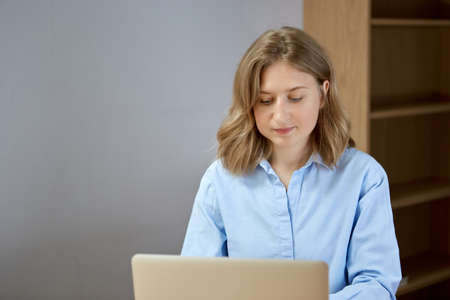 Close up portrait of a beautiful young woman looking at laptop screen. Work at home.