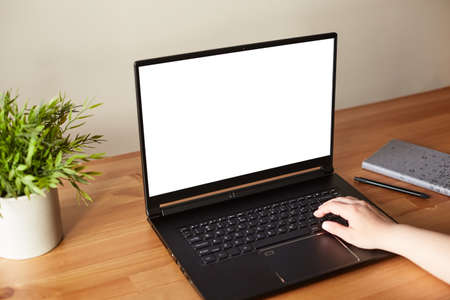 View of woman hands working on laptop with blank white screen standing on the wooden office desk....