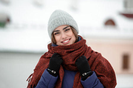Portrait of a young happy woman enjoying winter wearing scarf and knitted hat. Smiling girl in a colorful shawl looking at camera.の写真素材