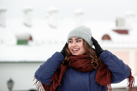 Portrait of a young happy woman enjoying winter wearing scarf and knitted hat. Smiling girl in a colorful shawl looking at camera.の写真素材