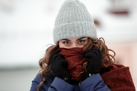 Closeup portrait of a young happy woman enjoying winter wearing scarf and knitted hat. Smiling girl in a colorful shawl looking at camera.の写真素材