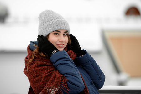 Portrait of a young happy woman enjoying winter wearing scarf and cap. Smiling girl in a colorful shawl looking at camera.の写真素材