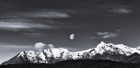 the moon emerging from a cloudy sky overhanging the snowy Alpsの写真素材