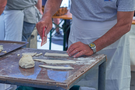 Close-up of a man kneading dough on a floured surface, wearing an apron. Traditional baking scene with raw dough and utensils, capturing the artisanal cooking process.の写真素材