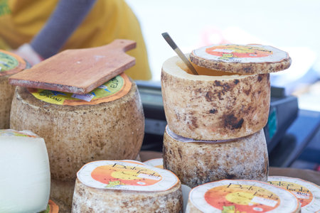 Artisan cheese sits beautifully arranged on wooden boards at a vibrant market. The setting features warm sunshine and lively interactions among visitors enjoying the offerings.の写真素材